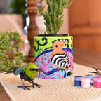 A colorful hand-painted paint-by-numbers planter with a hoopoe and pink  design, holding a green succulent.